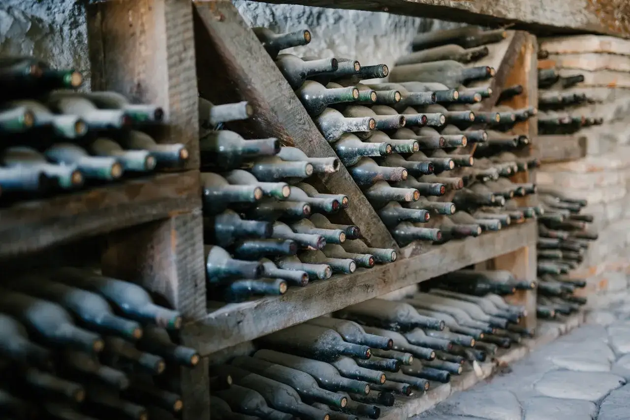 Des bouteilles de vin rouge poussiéreuses, empilées sur des étagères en bois rustiques, témoignant d'une longue conservation.