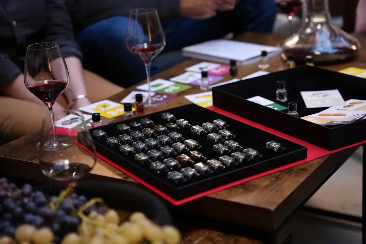 Dégustation de vin rouge : verres, carafes, grappes de raisin et petites fioles d'arômes sur une table en bois.