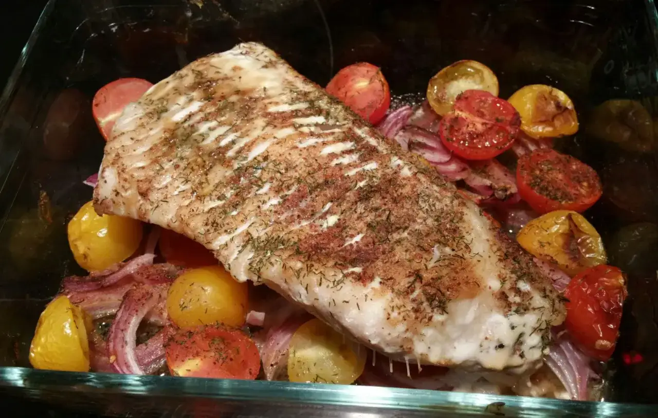 Délicieux filet de loup au four, parfumé au vin blanc, accompagné de tomates cerises et d'oignons rouges rôtis.