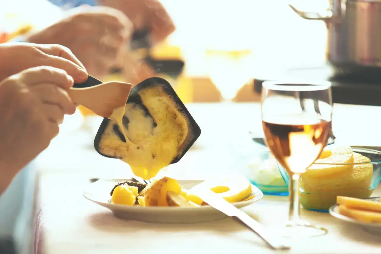 Raclette fondue versée sur des pommes de terre, accompagnée d'un verre de Bourgogne Aligoté.