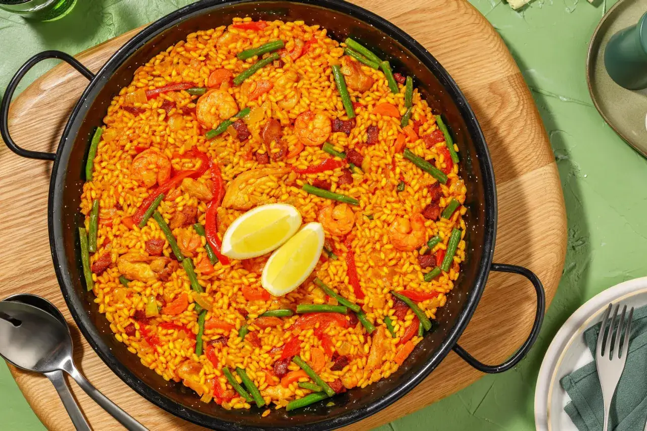 Un plat de riz fa&ccedil;on paella, garni de crevettes, poulet, chorizo, poivrons et haricots verts, avec deux quartiers de citron.