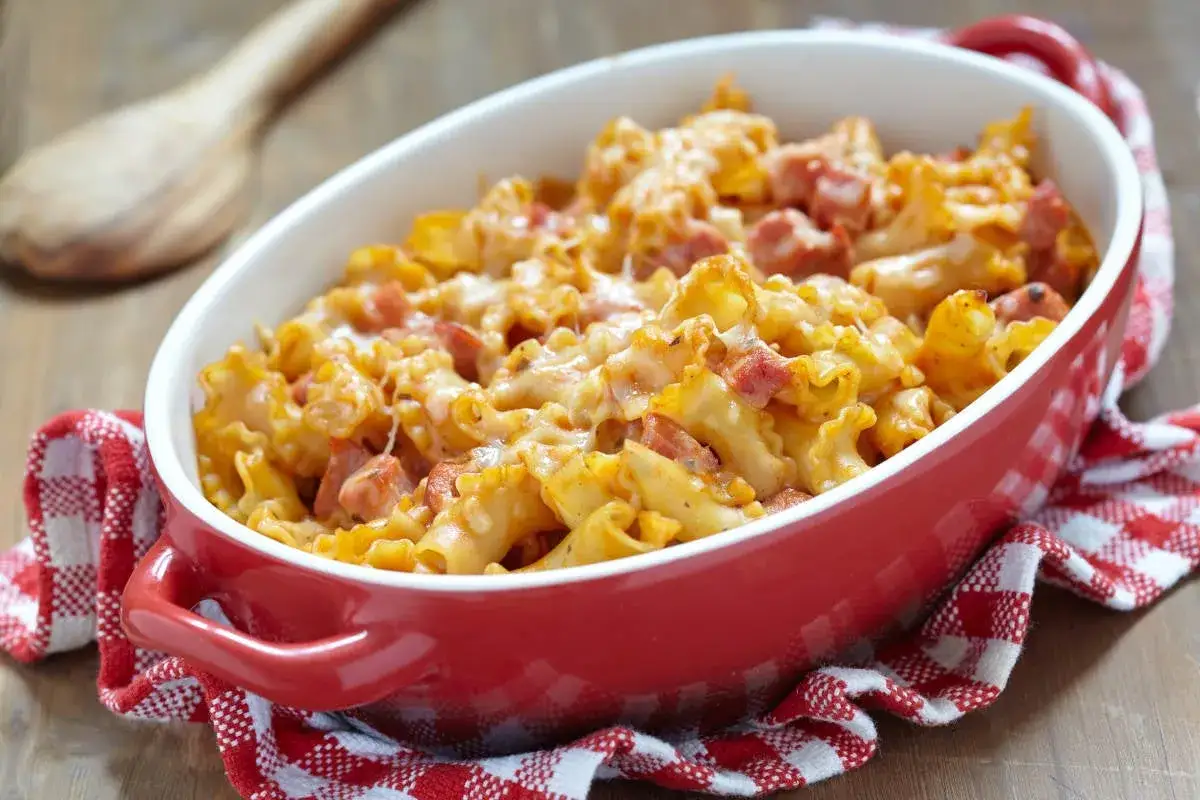 Un plat réconfortant de gratin de pâtes au jambon, gratiné au fromage fondant, servi dans un plat rouge.