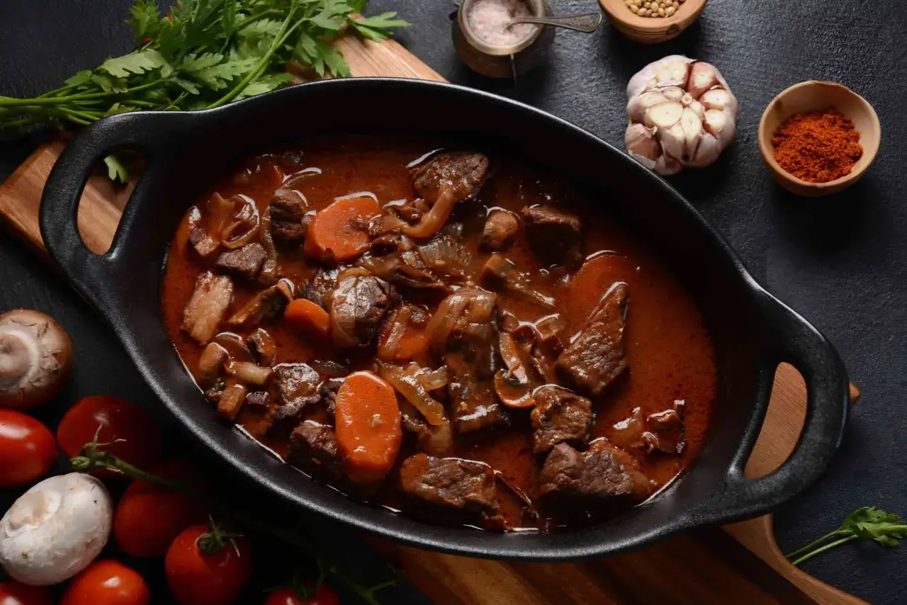 Un plat mijoté de bœuf bourguignon traditionnel, avec des carottes, des oignons et des champignons, prêt à être dégusté.