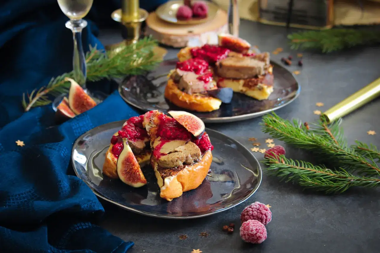 Pain perdu festif garni de foie gras, figues et framboises, sur fond sombre avec des branches de sapin.