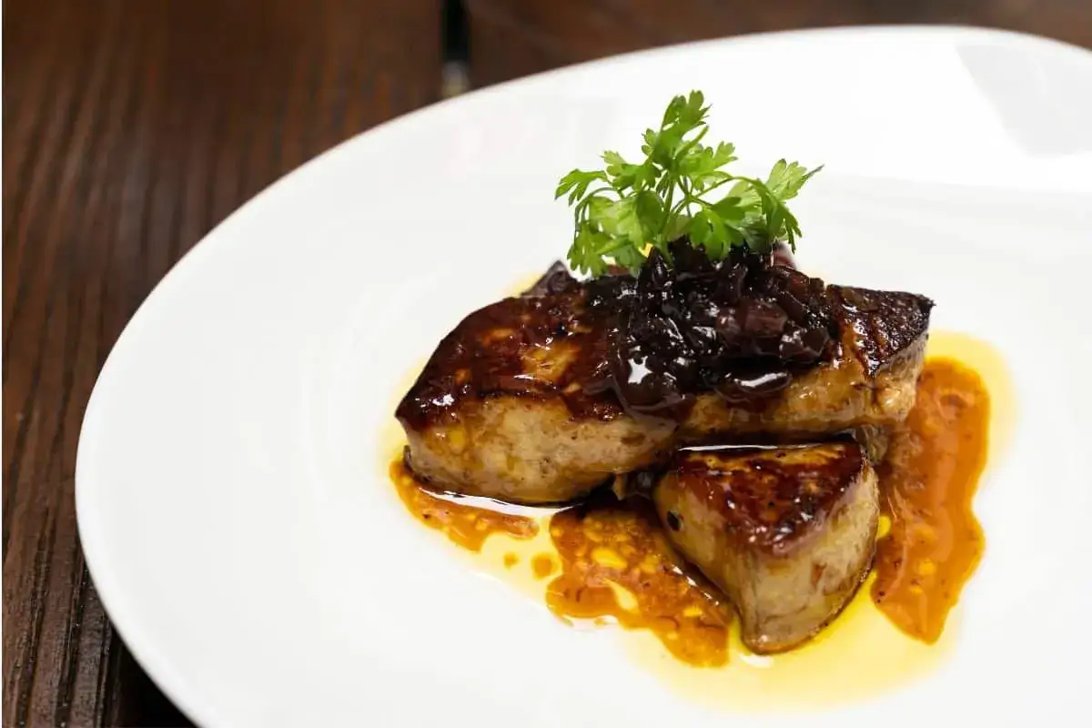 Délicieux foie gras poêlé, nappé d'une sauce ambrée et garni d'une compotée sombre et de persil frais.