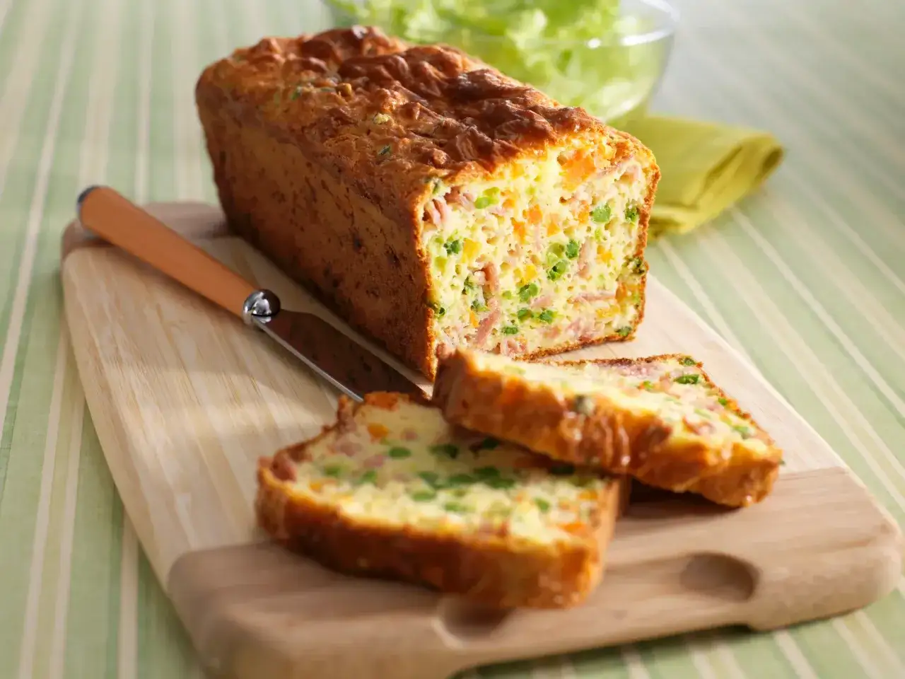 Un délicieux cake aux légumes, coupé en tranches, révèle des morceaux de carottes, petits pois et jambon. Un couteau est posé à côté.
