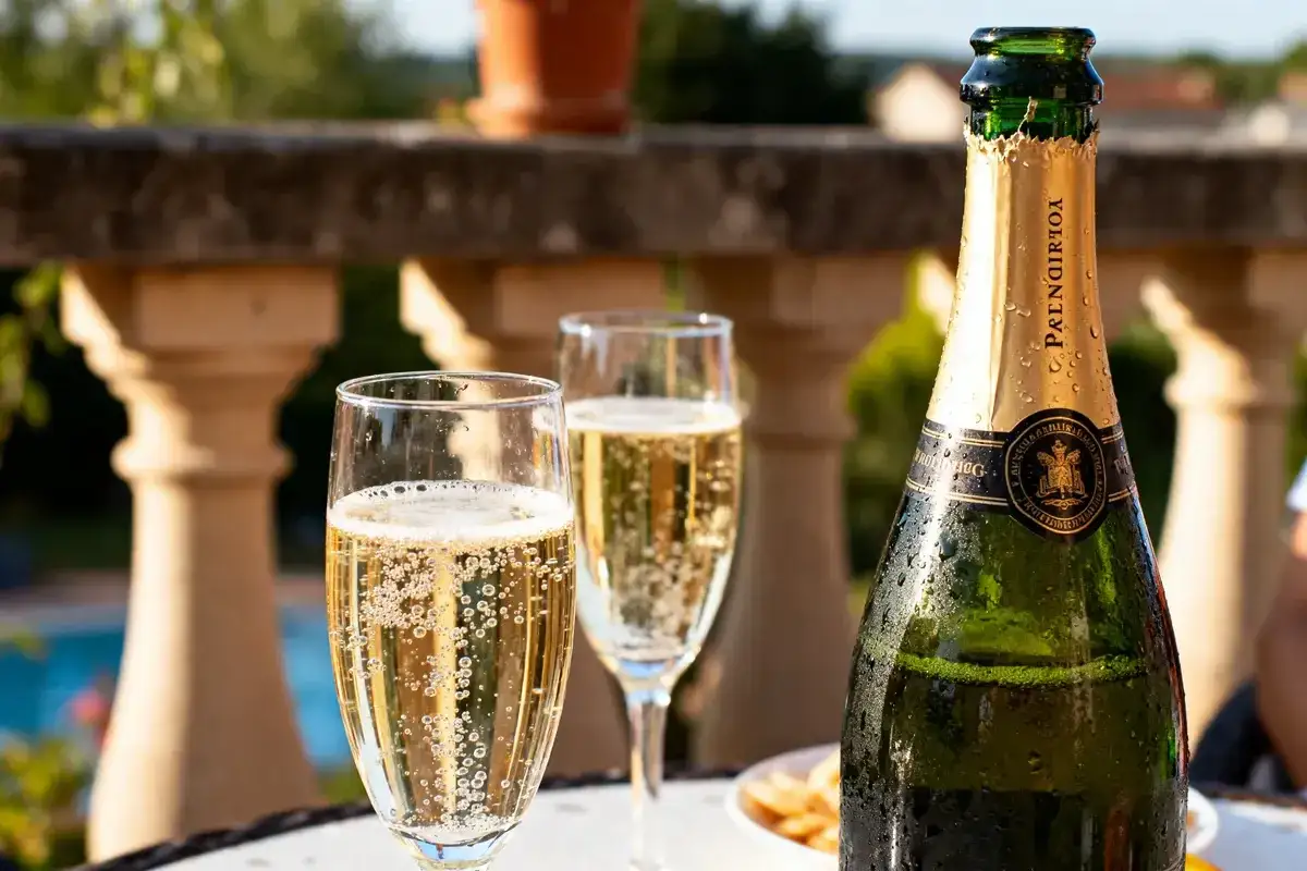 Bouteille de champagne et deux flûtes pétillantes sur une terrasse ensoleillée. Idéal pour savoir à quelle température boire le champagne.