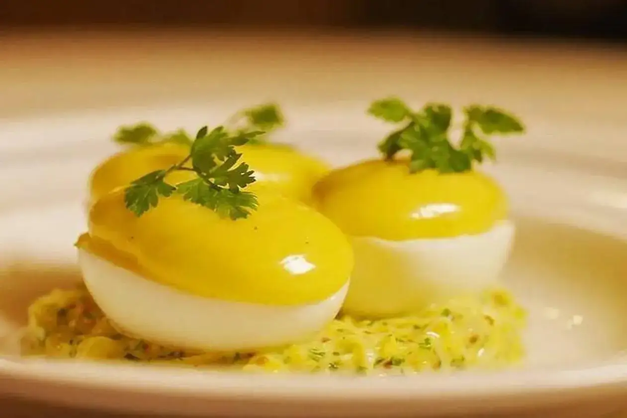Trois moitiés d'oeuf mayonnaise, garnies de persil frais, reposent sur une sauce crémeuse.