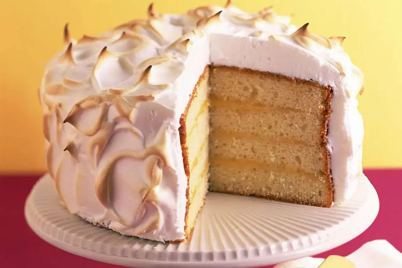 Gâteau moelleux à la crème, recouvert d'une meringue italienne dorée et aérienne. Une tranche révèle ses couches généreuses.