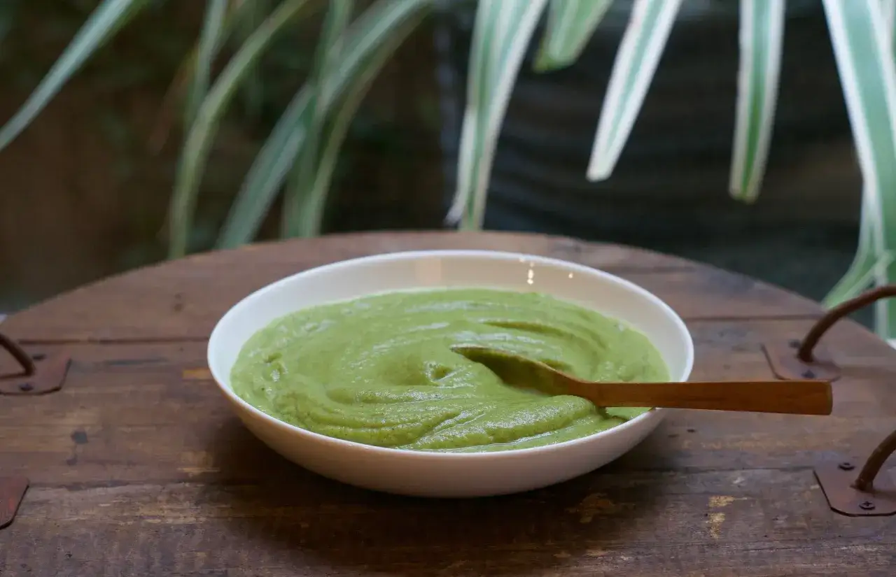 Un bol de purée de brocolis onctueuse, avec une cuillère en bois. Un plat sain et coloré, prêt à être dégusté.