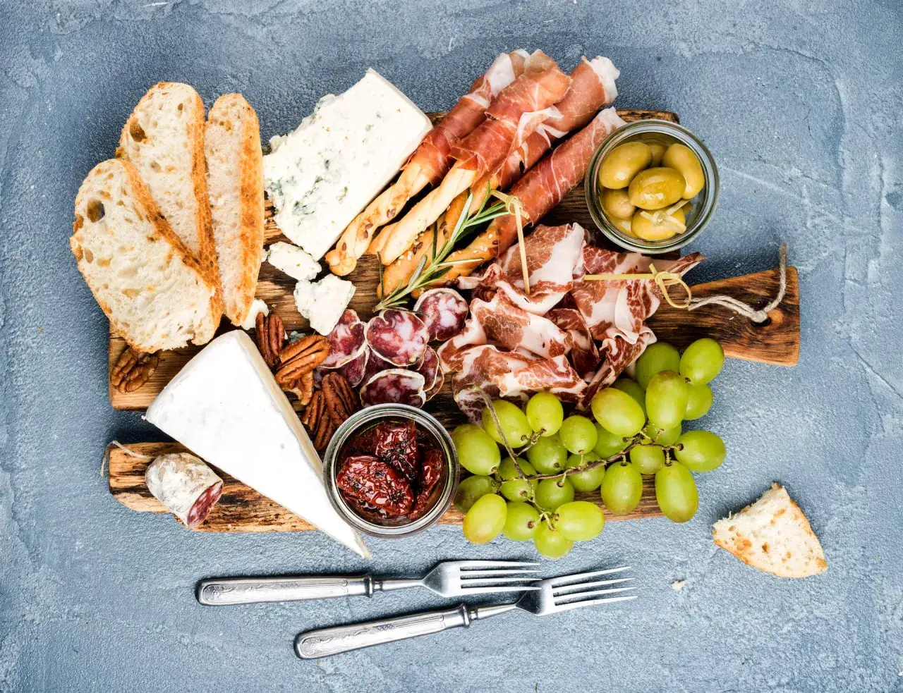Plateau gourmand : assortiment de fromage, charcuterie, olives, raisins et pain. Parfait pour accompagner un verre de vin blanc ou rouge.