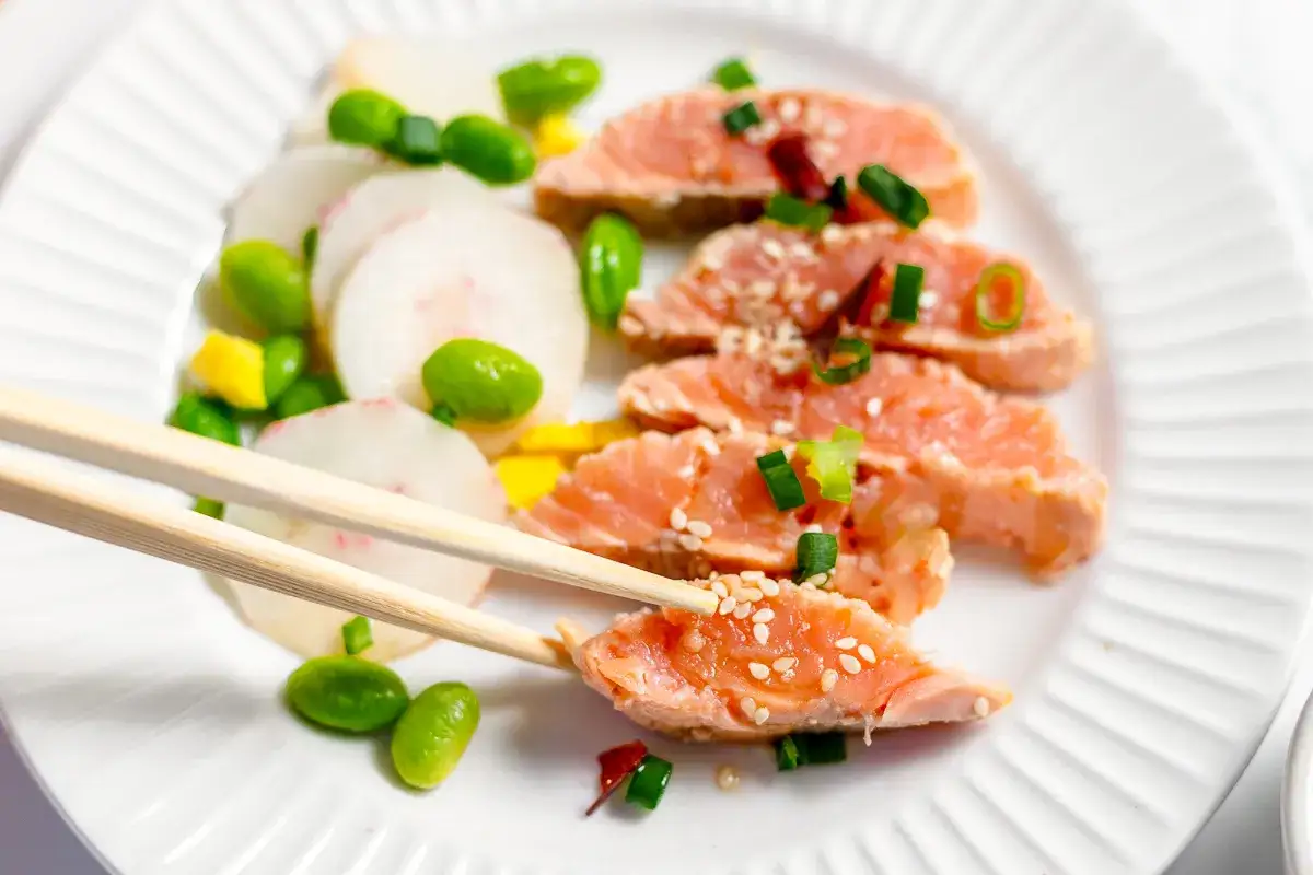 Délicieux tataki de saumon, garni de graines de sésame et d'oignons verts, servi avec des radis et des edamames.