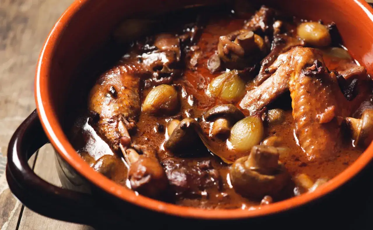Un plat de coq au vin mijoté, avec des morceaux de poulet, des champignons et des petits oignons. Parfait pour savoir que boire avec un coq au vin.