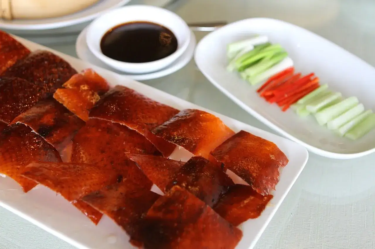 Canard laqué recette : peau croustillante et dorée, servie avec des bâtonnets de concombre, de poireau et une sauce foncée. Un délice !