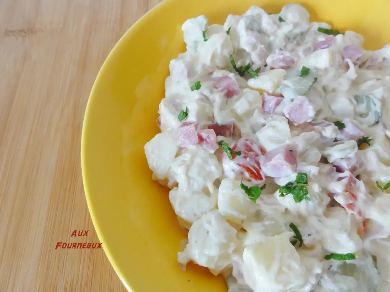 Salade piémontaise maison crémeuse, garnie de dés de jambon, pommes de terre et persil frais, servie dans un plat jaune vif.