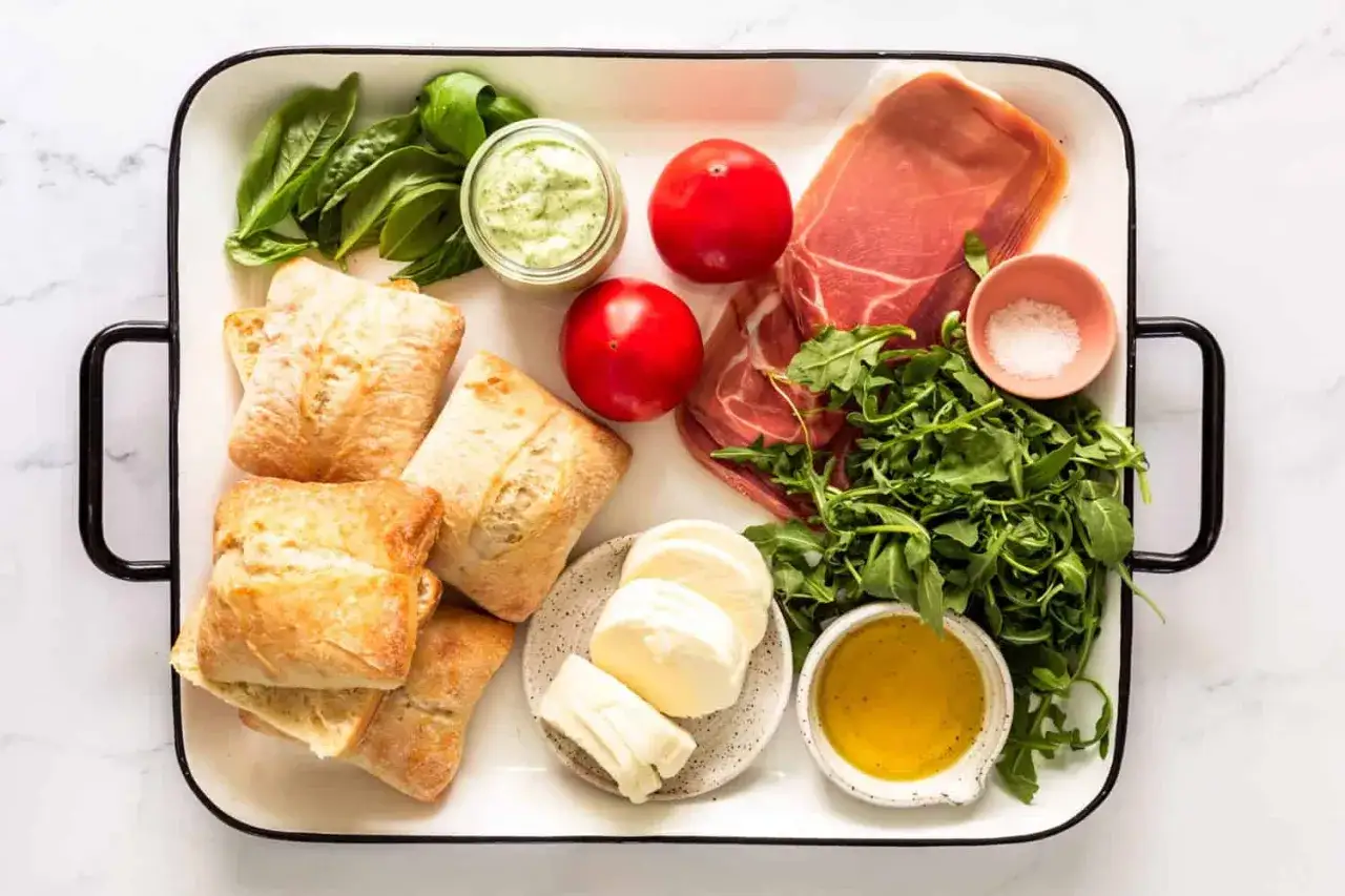Ingrédients pour un délicieux sandwich italien : pains ciabatta, prosciutto, mozzarella, tomates, roquette, basilic, sauce et sel.