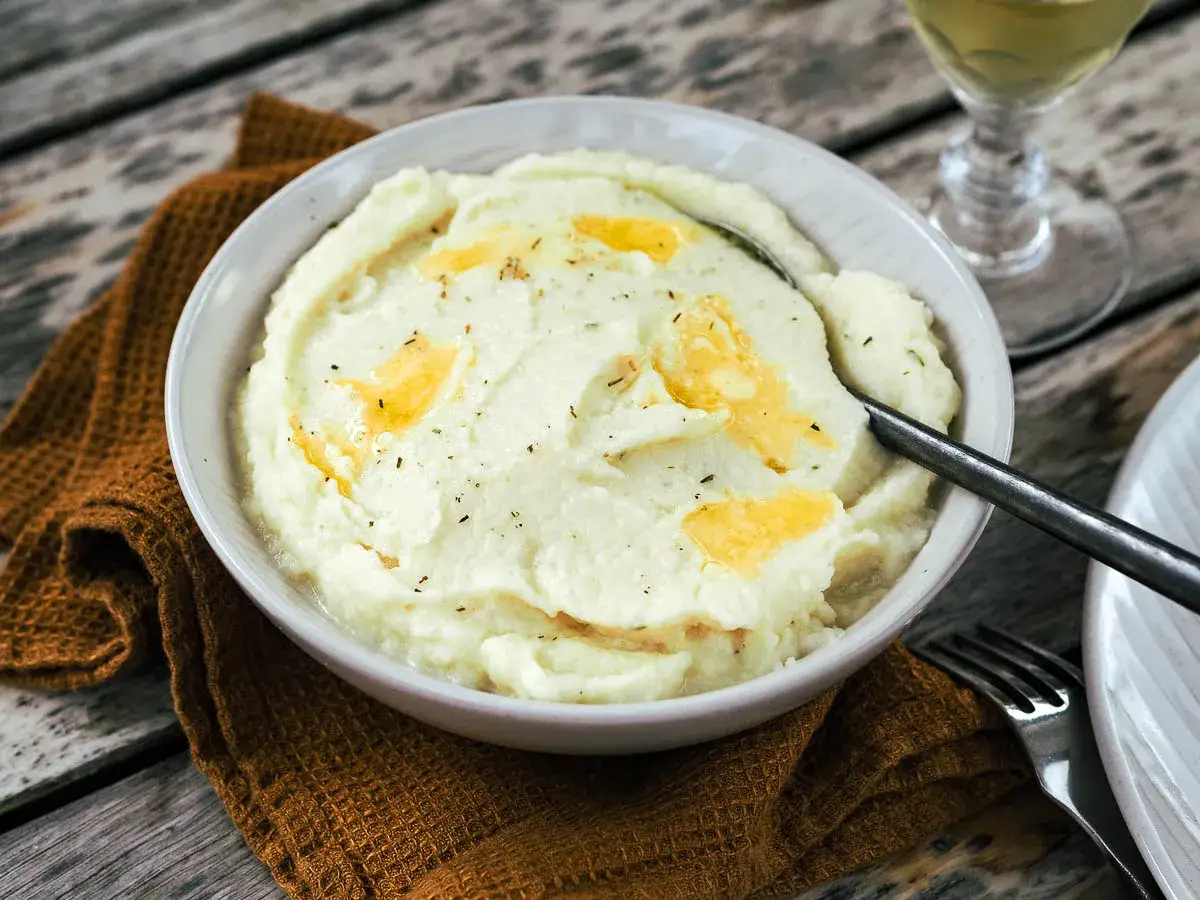 Un bol de purée de céleri onctueuse, garnie de beurre fondu et d'herbes, prête à être dégustée.