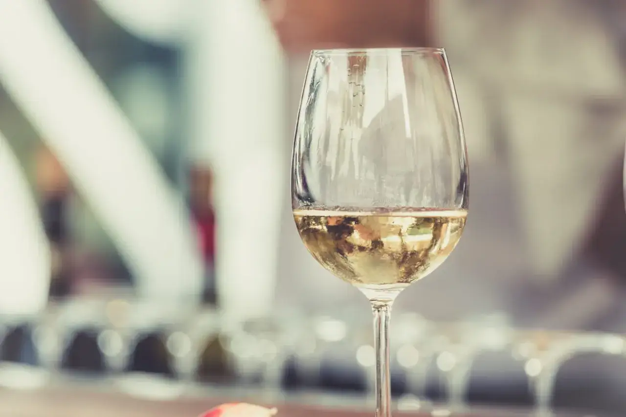 Un verre de vin blanc, peut-être un sauvignon sec ou moelleux, reflète la lumière. En arrière-plan, d'autres verres attendent.