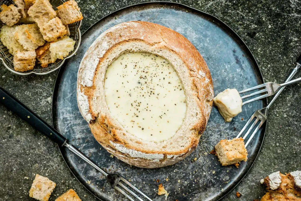 Une généreuse fondue savoyarde dans un pain rond, accompagnée de croûtons et de fourchettes pour un festin convivial.