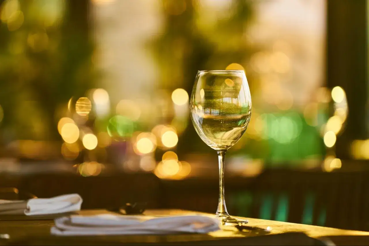 Un verre de vin blanc sur une table, avec des lumières douces en arrière-plan. Un tableau qui évoque le temps de garde des vins blancs.