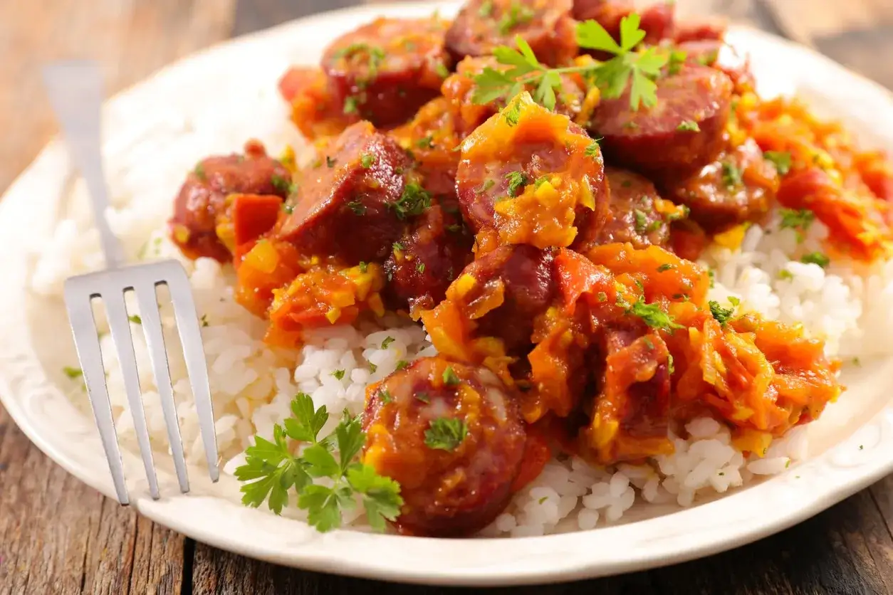 Assiette de riz blanc garnie de rougail saucisse, plat r&eacute;unionnais savoureux, avec une touche de persil frais.