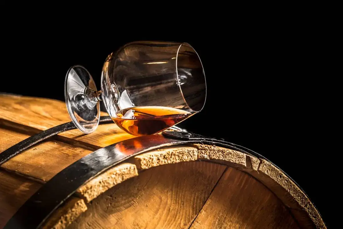 Verre de cognac renversé sur un fût de bois. Le vin est-il un spiritueux ? La question se pose devant cette boisson ambrée.