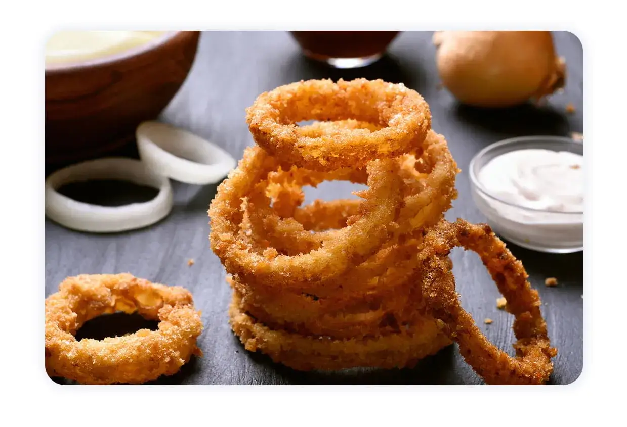 Pile de délicieux oignon rings dorés et croustillants, accompagnés de sauce et d'oignons frais.
