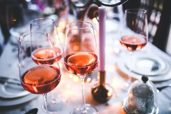 Verres remplis de bon vin rose, prêts pour une célébration festive avec des bougies et des lumières douces.