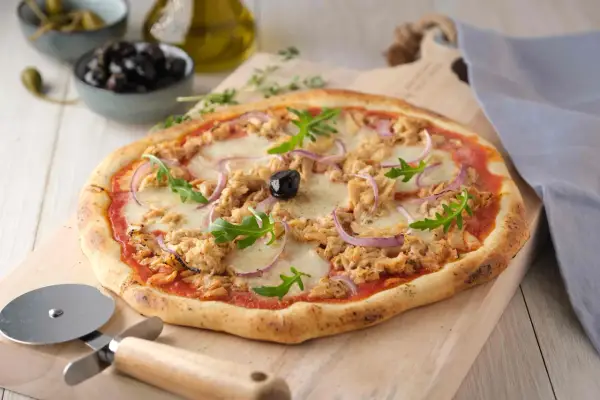 Une délicieuse pizza au thon, garnie d'oignons rouges, de roquette et d'une olive noire, prête à être découpée.