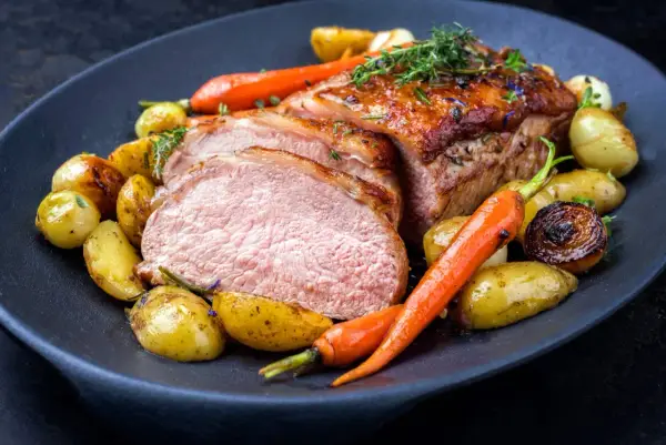 Délicieuse côte de veau barbecue, tranchée et servie avec des pommes de terre rôties et des carottes glacées, garnie d'herbes fraîches.